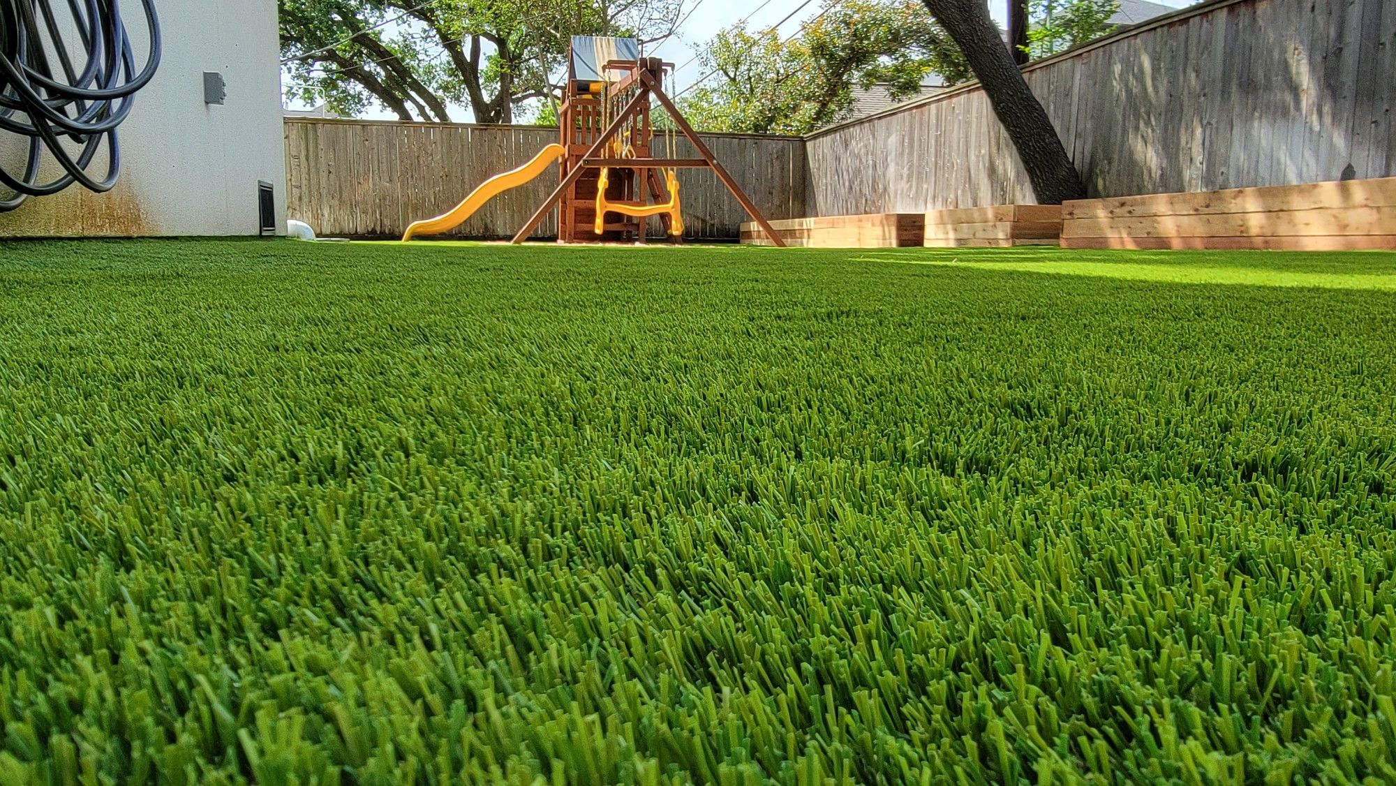 Close view of dense, vivid artificial turf in a finished backyard with a play structure